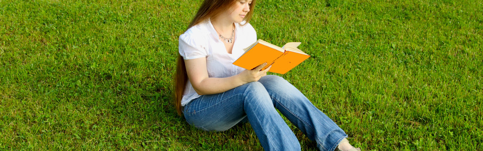 blond girl reading red book over the grass